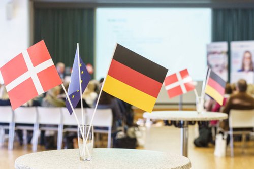 Dekoratives Bild – Ein Tisch mit einem Glas, in welchem die deutsche, die dänische und die europäische Flagge zu sehen sind